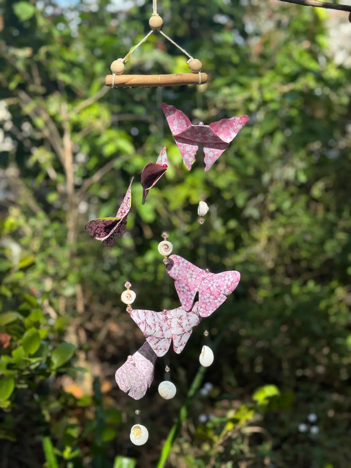 Butterfly-shaped wind chime with pink and purple patterns hanging against a green outdoor background.